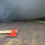 Eine Feuerwehraxt liegt auf dem Boden einer vernebelten Lagerhalle